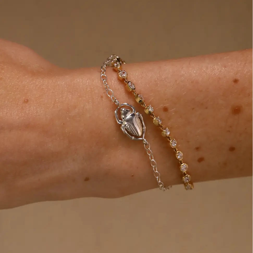 Bracelet with a scarab charm on a wrist against a beige background
