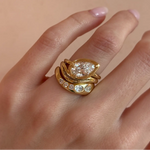Gold ring with a pear-shaped diamond on a hand against a beige background