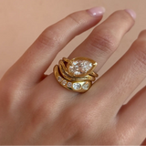 Gold ring with a pear-shaped diamond on a hand against a beige background