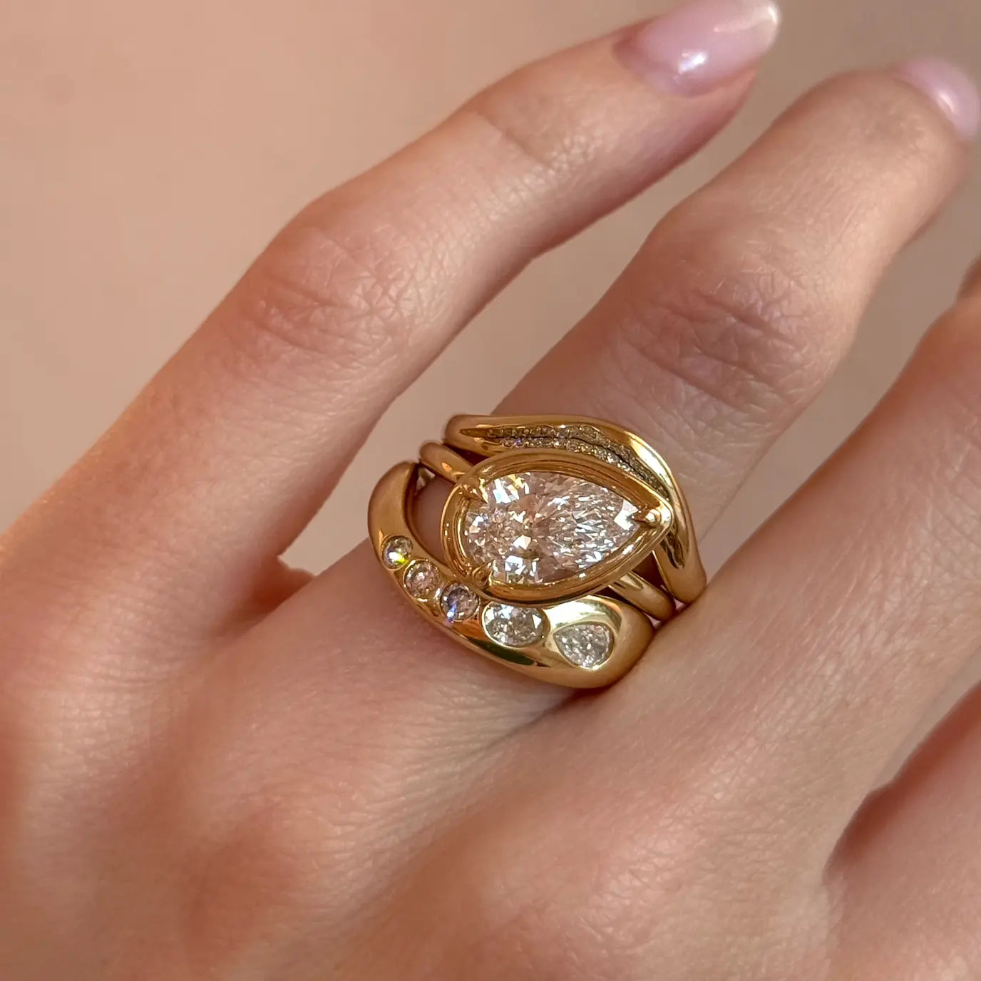 Gold ring with a large diamond on a finger against a beige background