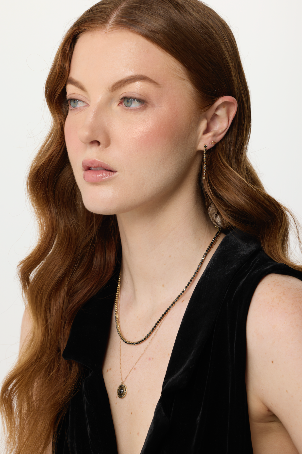 Woman wearing a black sleeveless top and gold necklaces on a white background