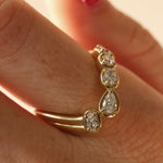 close up of woman's finger with a yellow gold asymmetrical ring that features different diamond cuts (pear oval, cushion)