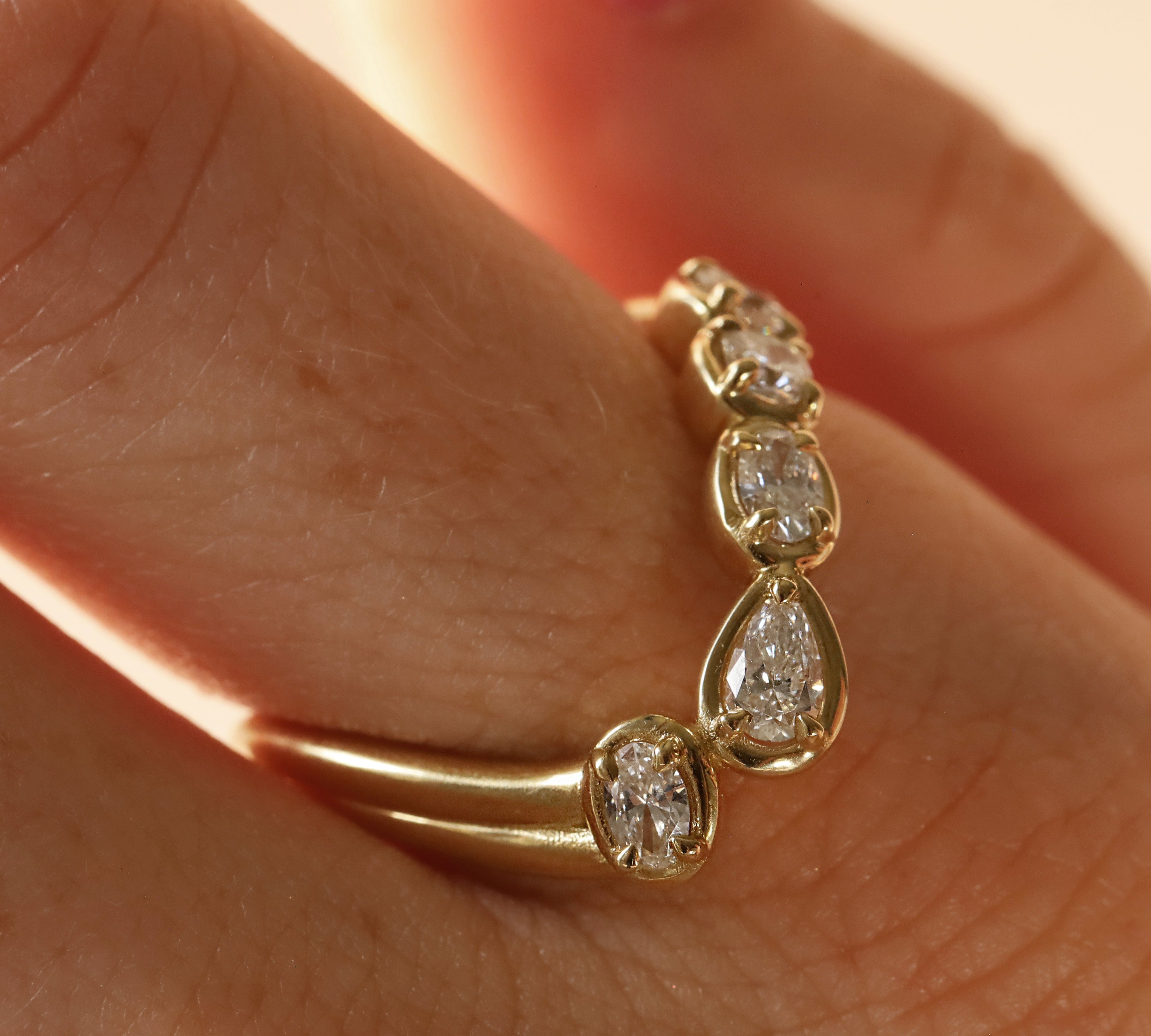 close up of woman's finger with a yellow gold asymmetrical ring that features different diamond cuts (pear oval, cushion)