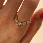close up of woman's finger with a yellow gold asymmetrical ring that features different diamond cuts (pear oval, cushion)