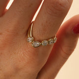 close up of woman's finger with a yellow gold asymmetrical ring that features different diamond cuts (pear oval, cushion)