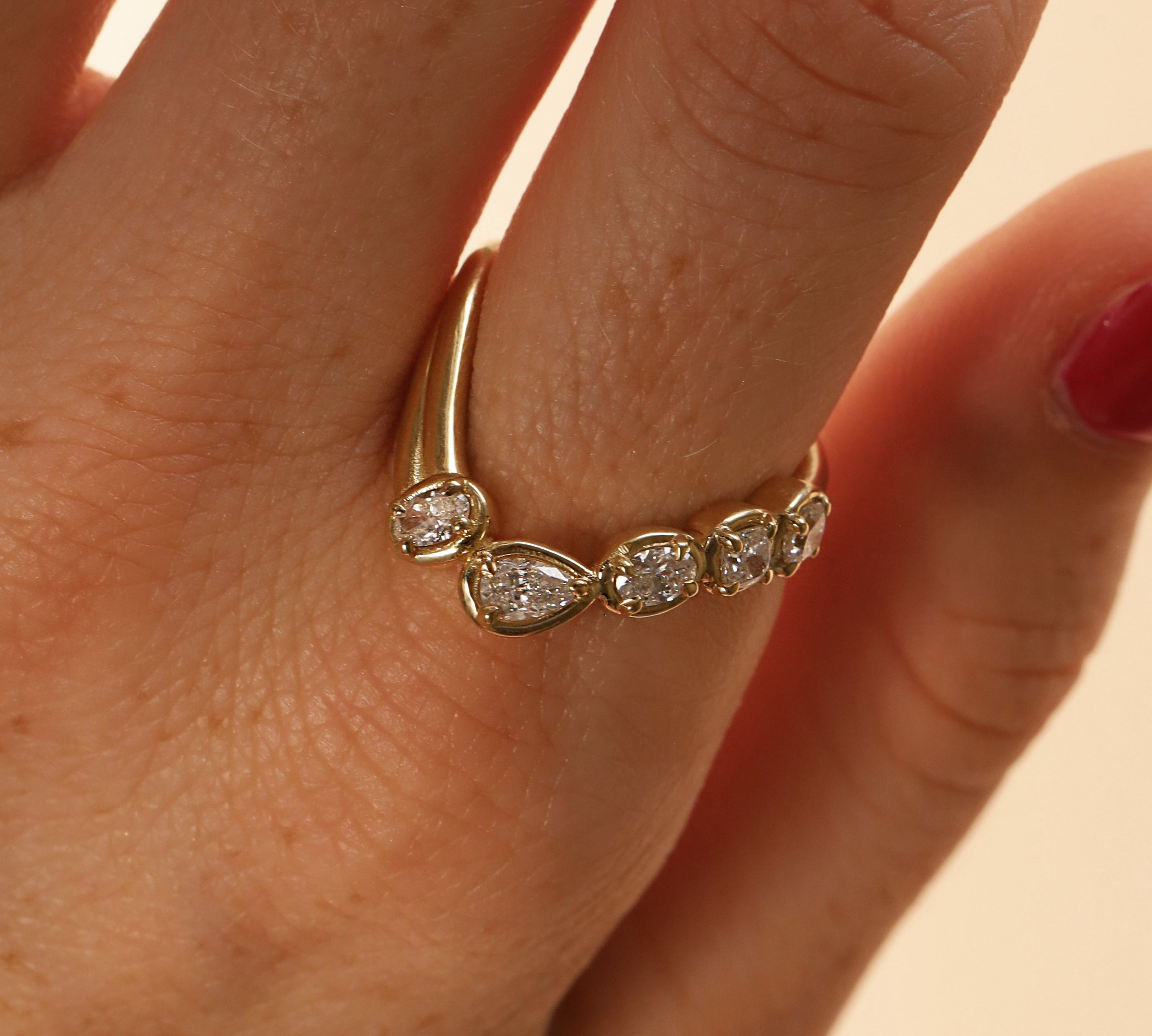 close up of woman's finger with a yellow gold asymmetrical ring that features different diamond cuts (pear oval, cushion)