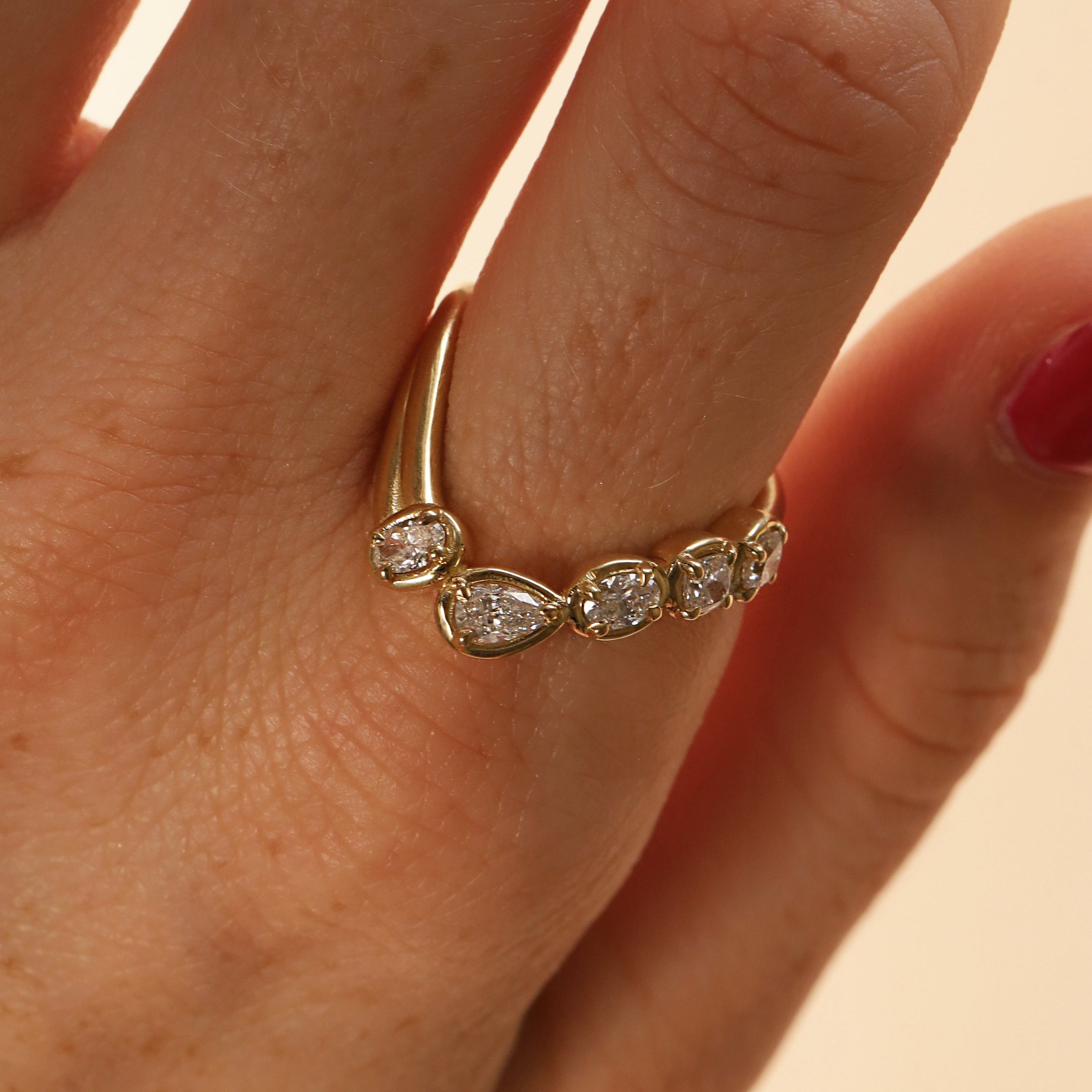 close up of woman's finger with a yellow gold asymmetrical ring that features different diamond cuts (pear oval, cushion)