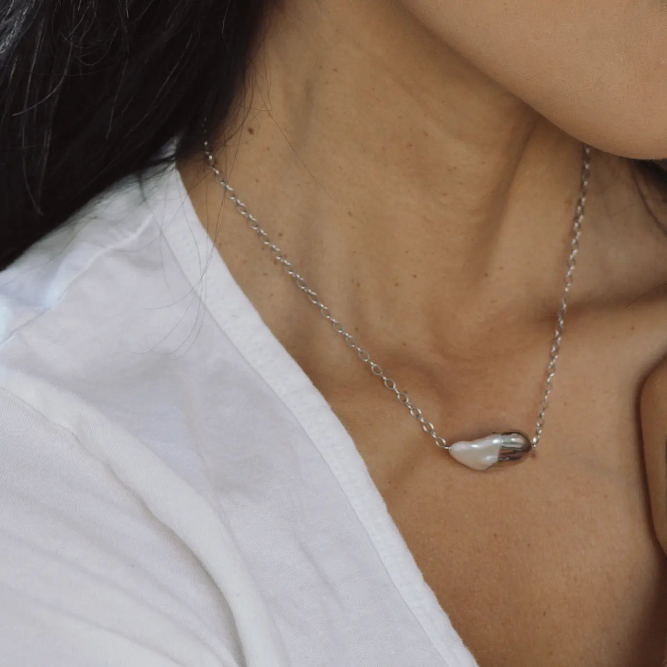 Close-up of a person wearing a silver necklace with a pearl pendant.