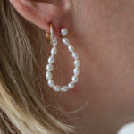 Pearl hoop earrings worn by a person with blonde hair.