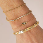 Close-up of a wrist wearing multiple gold bracelets with various designs on a neutral background.