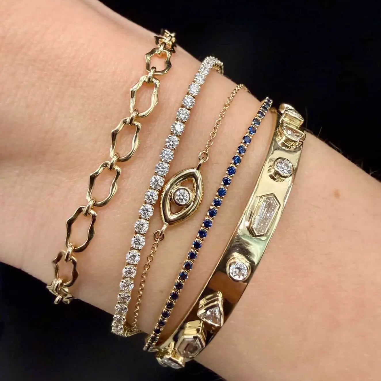 Close up of wrist with multiple gold and diamond bracelets stacked together