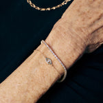 Close-up of an elderly person's wrist wearing a delicate gold bracelet with a small diamond on a dark background.