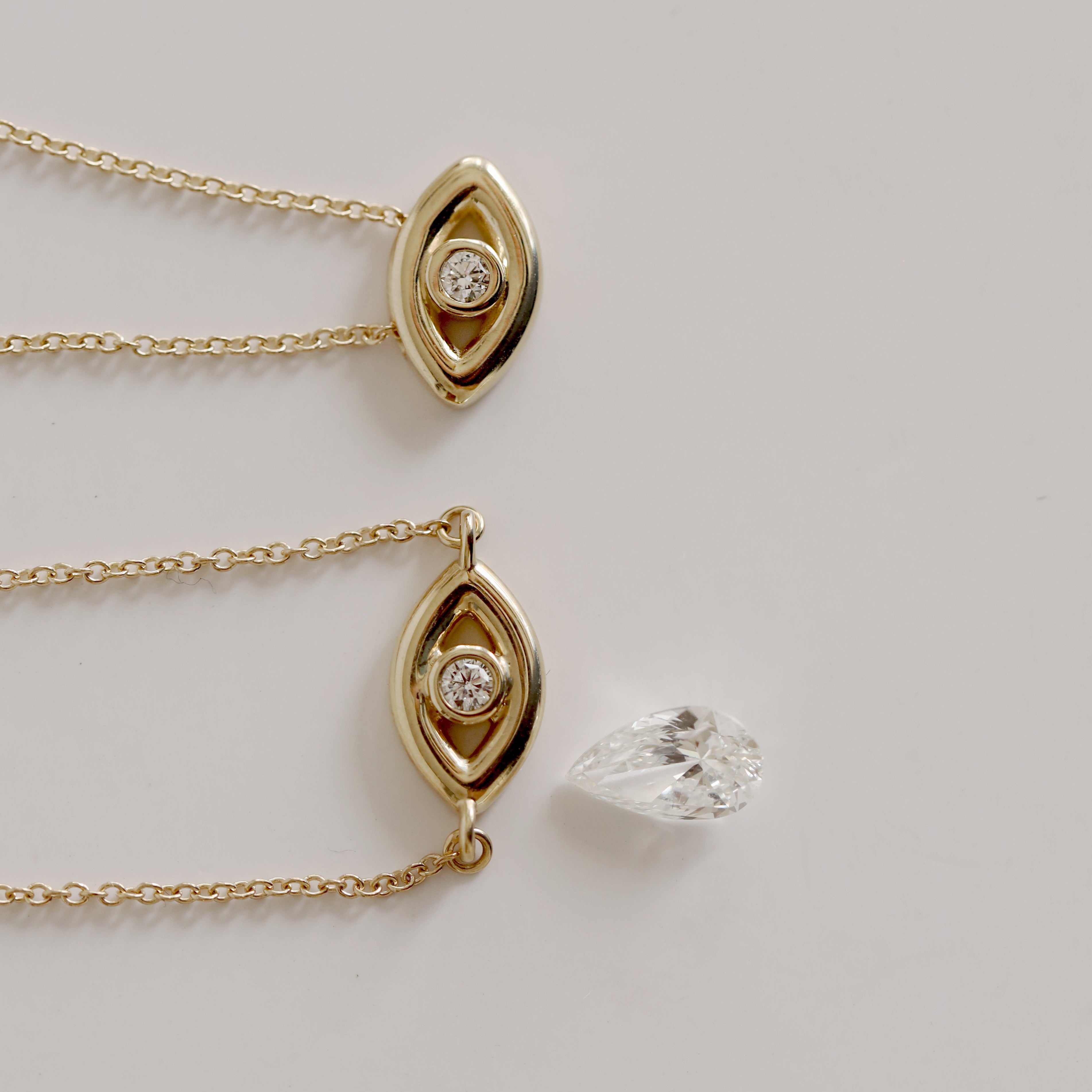 Gold necklace with teardrop-shaped pendant and diamond, alongside a loose diamond on a light gray background.