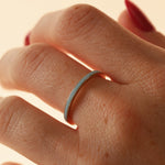 Close up of woman's hand wearing a dainty light blue enamel straight band on middle finger, against a neutral background