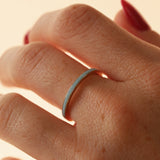 Close up of woman's hand wearing a dainty light blue enamel straight band on middle finger, against a neutral background