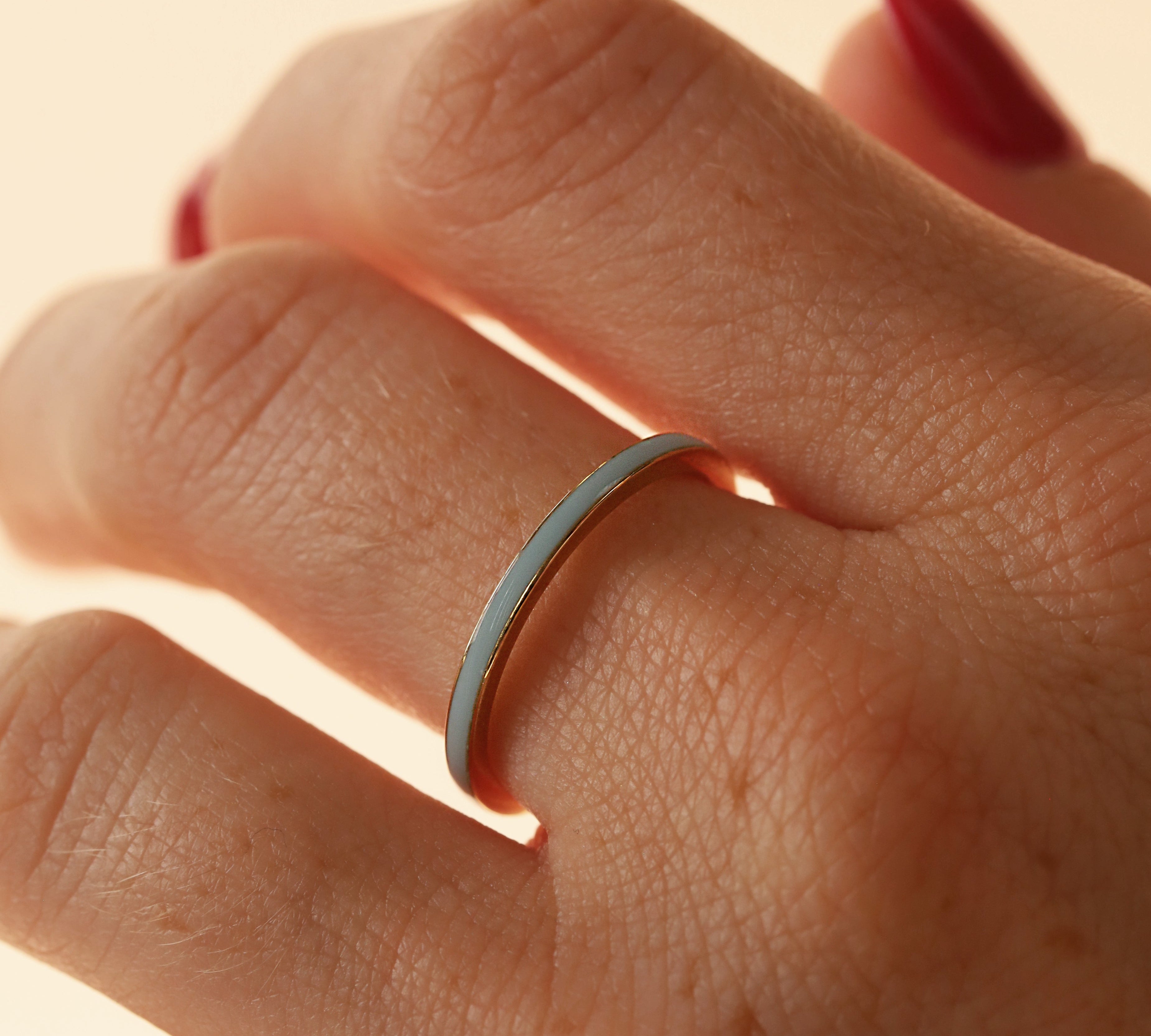 Close up of woman's hand wearing a dainty light blue enamel straight band on middle finger, against a neutral background
