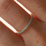 Close up of woman's hand wearing a dainty light blue enamel straight band on middle finger, against a neutral background