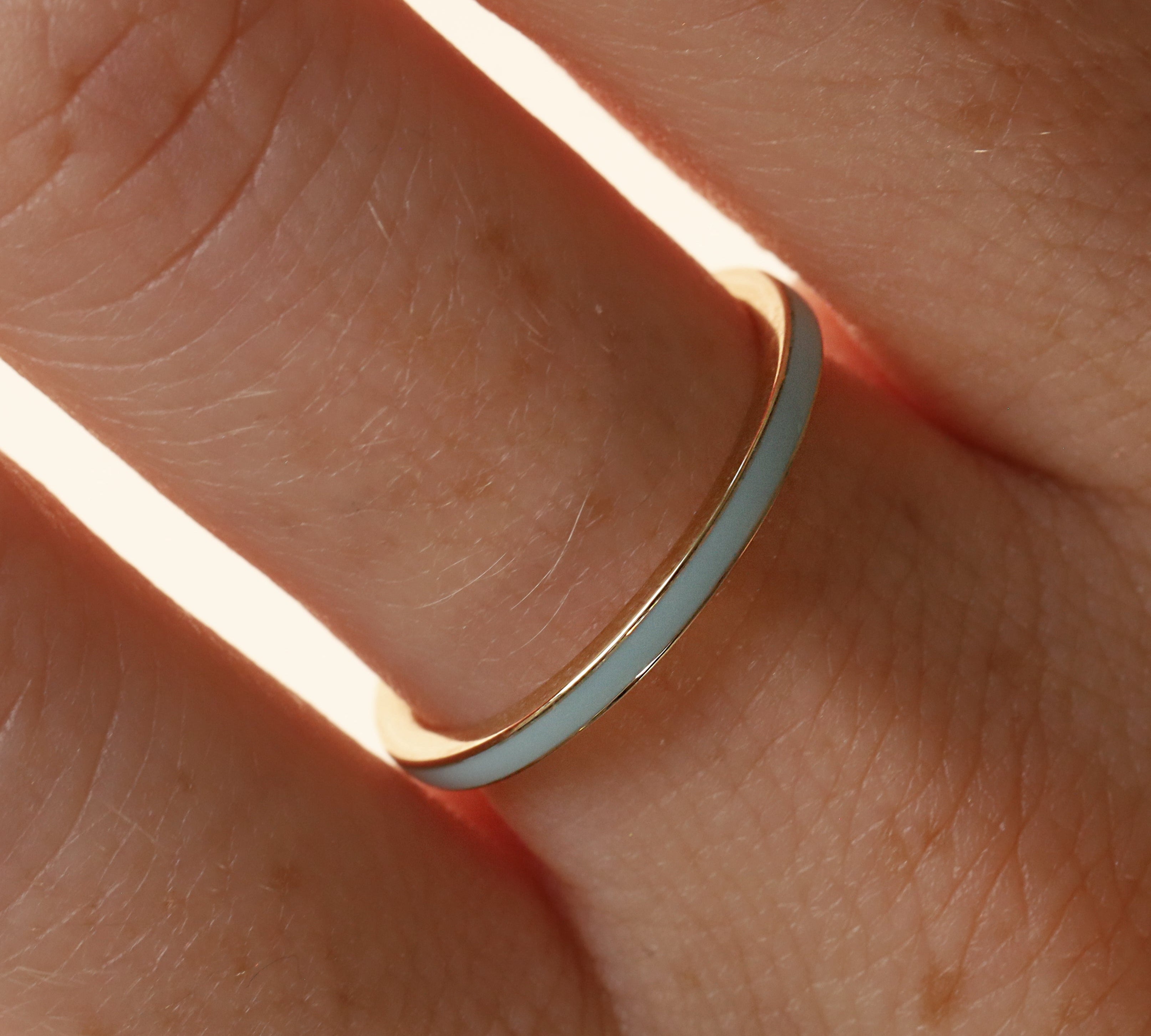 Close up of woman's hand wearing a dainty light blue enamel straight band on middle finger, against a neutral background