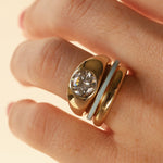 Close up of woman's hand wearing a dainty light blue enamel straight band, a domed solid gold band, and a gold bombe ring with a round diamond, against a neutral background.