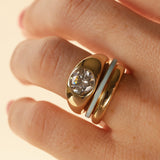 Close up of woman's hand wearing a dainty light blue enamel straight band, a domed solid gold band, and a gold bombe ring with a round diamond, against a neutral background.