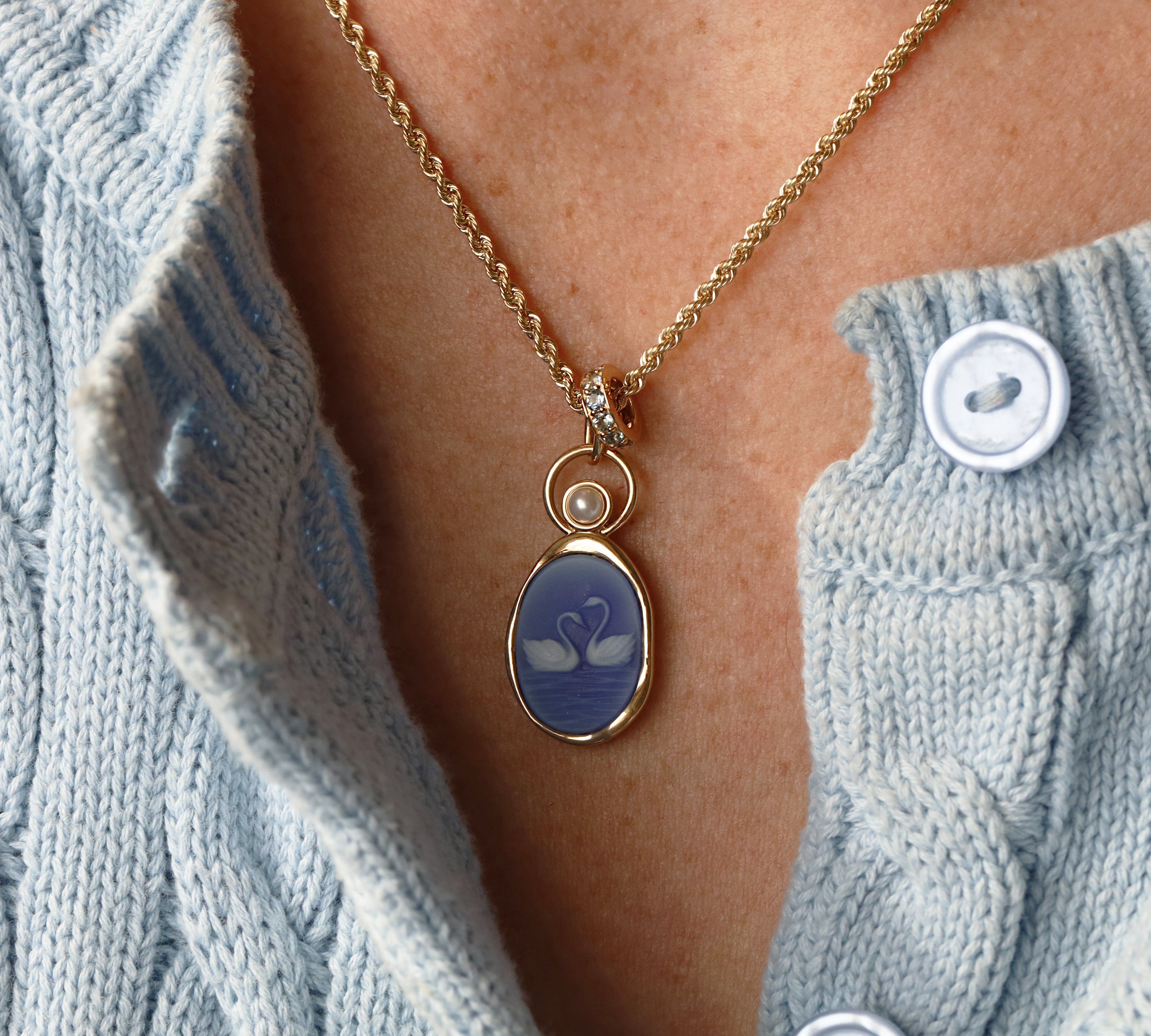 Swan Carving with 3.8mm Pearl Charm worn on the neck – two swans with necks forming a heart, carved in white on violet agate in 14k yellow gold, with a pearl floating in an open gold ring