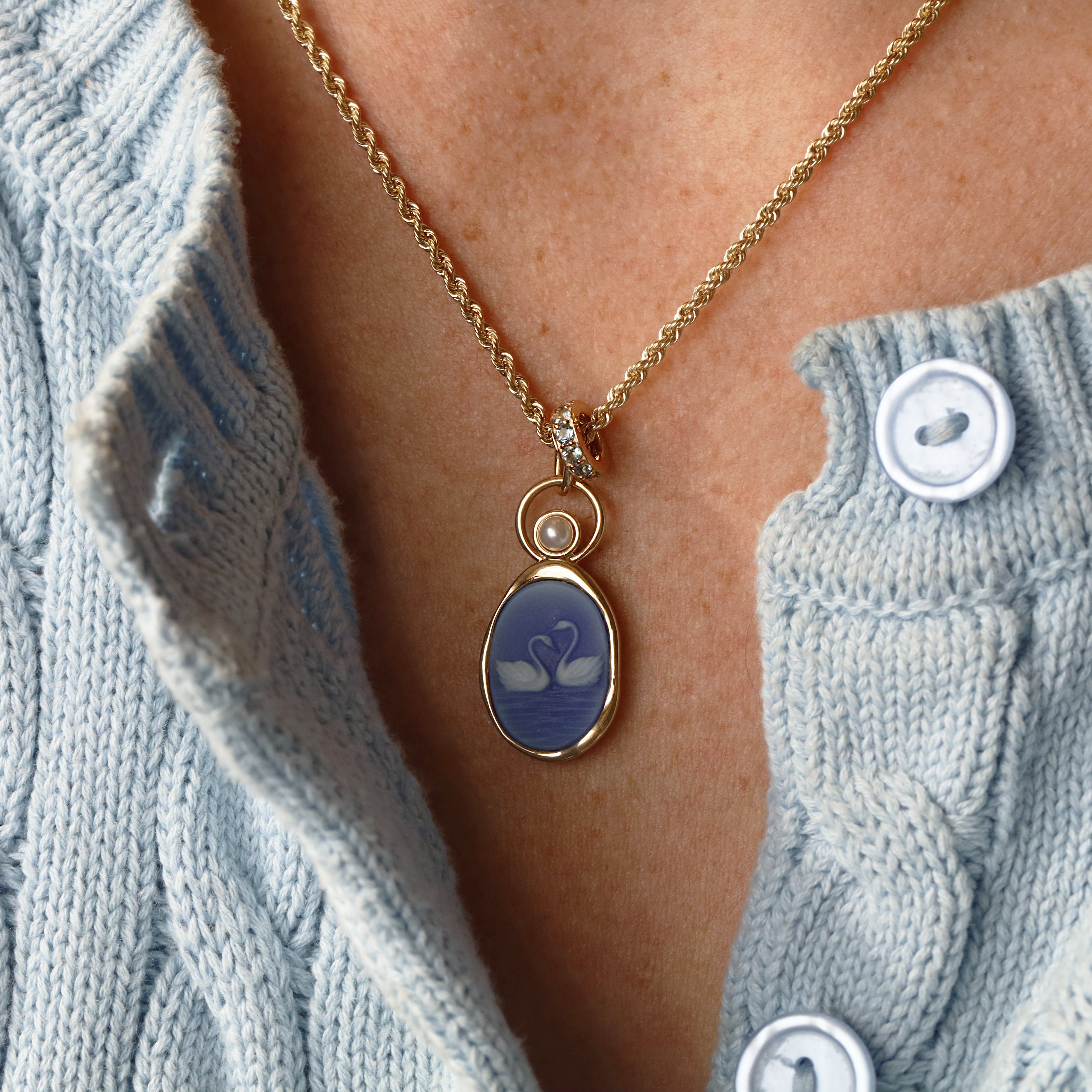 Swan Carving with 3.8mm Pearl Charm worn on the neck – two swans with necks forming a heart, carved in white on violet agate in 14k yellow gold, with a pearl floating in an open gold ring