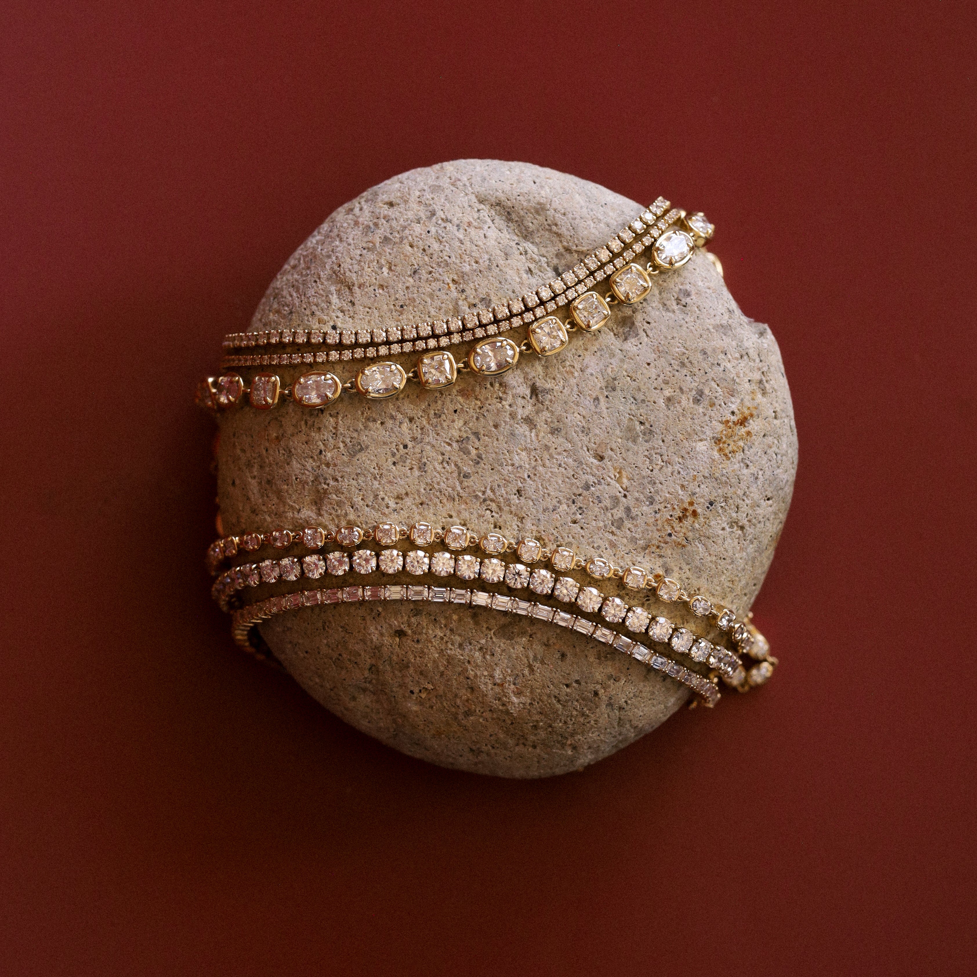 flatlay of stone with tennis bracelets styled on top of it to mimic a tennis ball design over a red/burgundy background