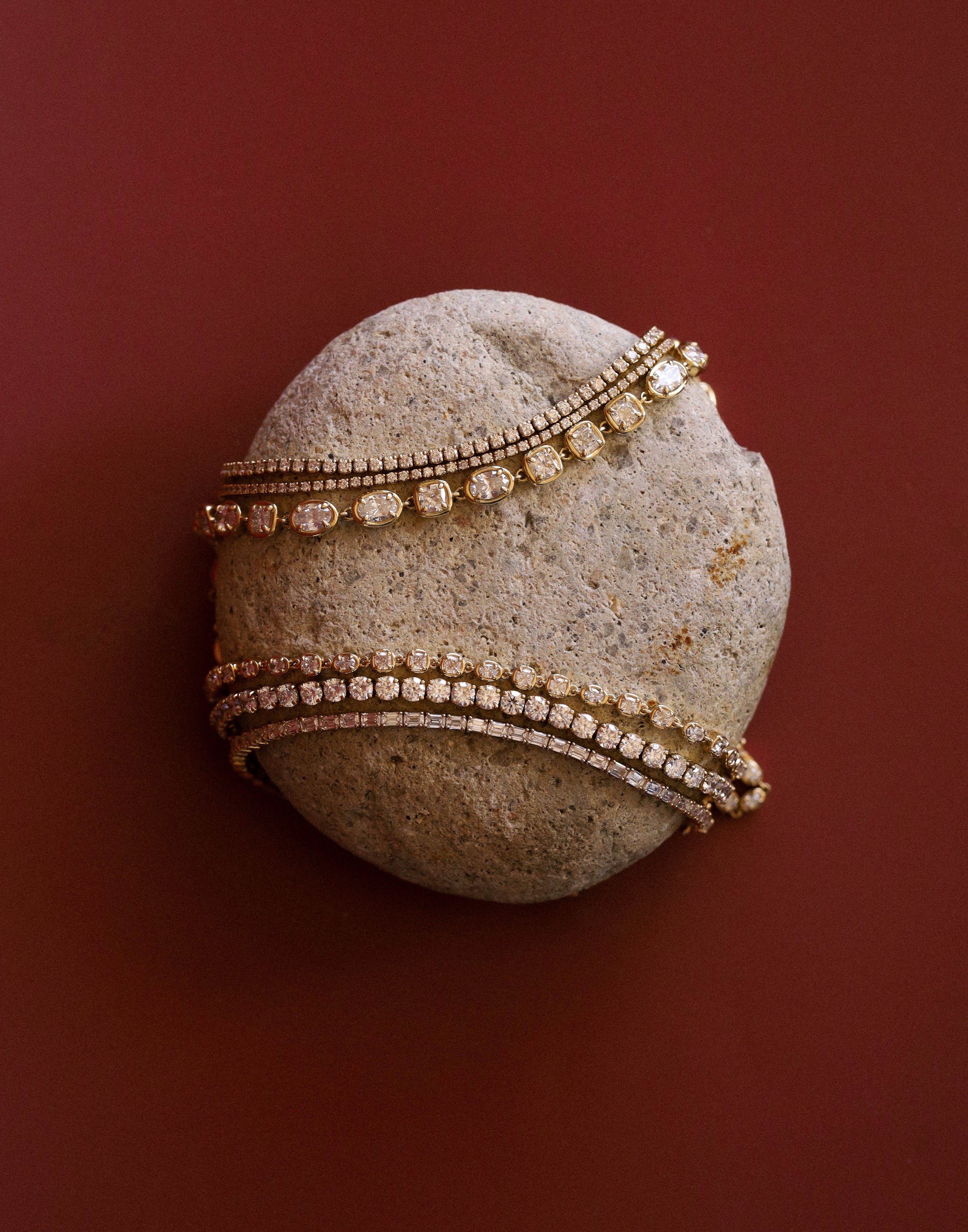 flatlay of stone with tennis bracelets styled on top of it to mimic a tennis ball design over a red/burgundy background