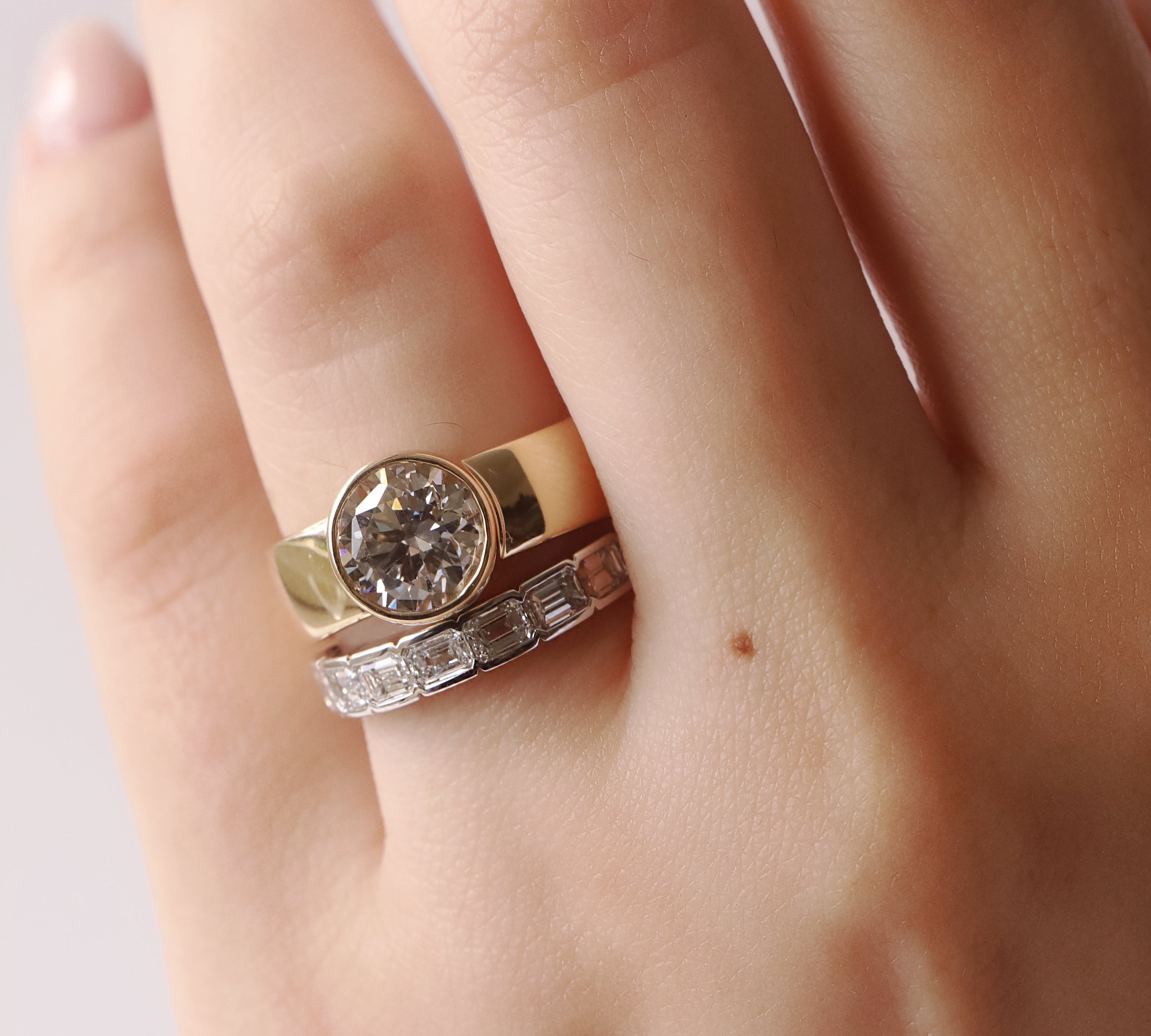 Close-up of a hand wearing two diamond rings on a light background