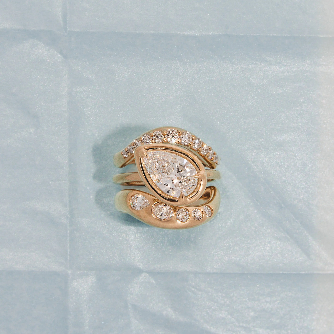 Yellow gold ring with pear-shaped diamond on a light blue textured background