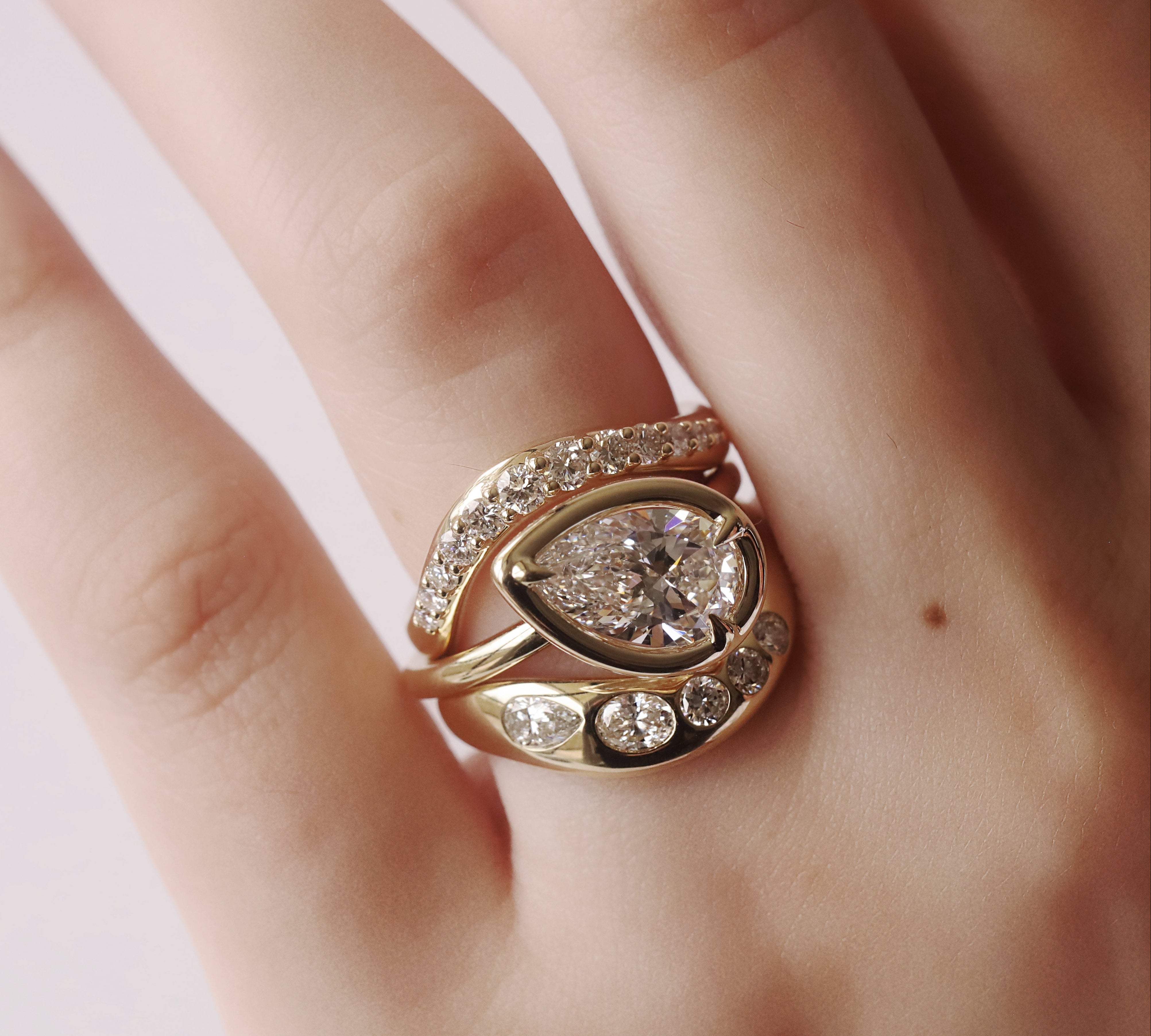 Rose gold ring with pear-shaped diamond on a hand against a light background