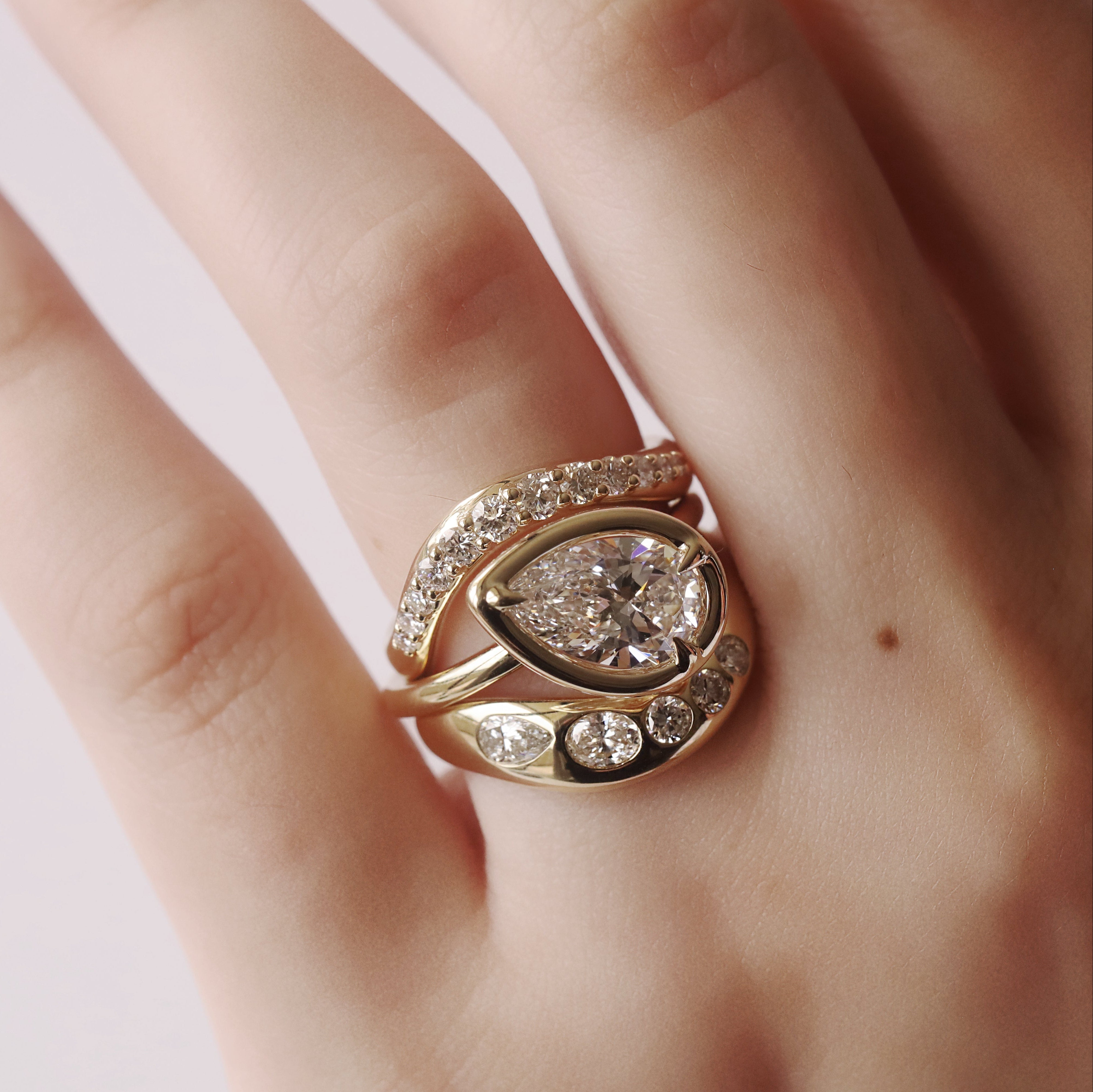 Rose gold ring with pear-shaped diamond on a hand against a light background