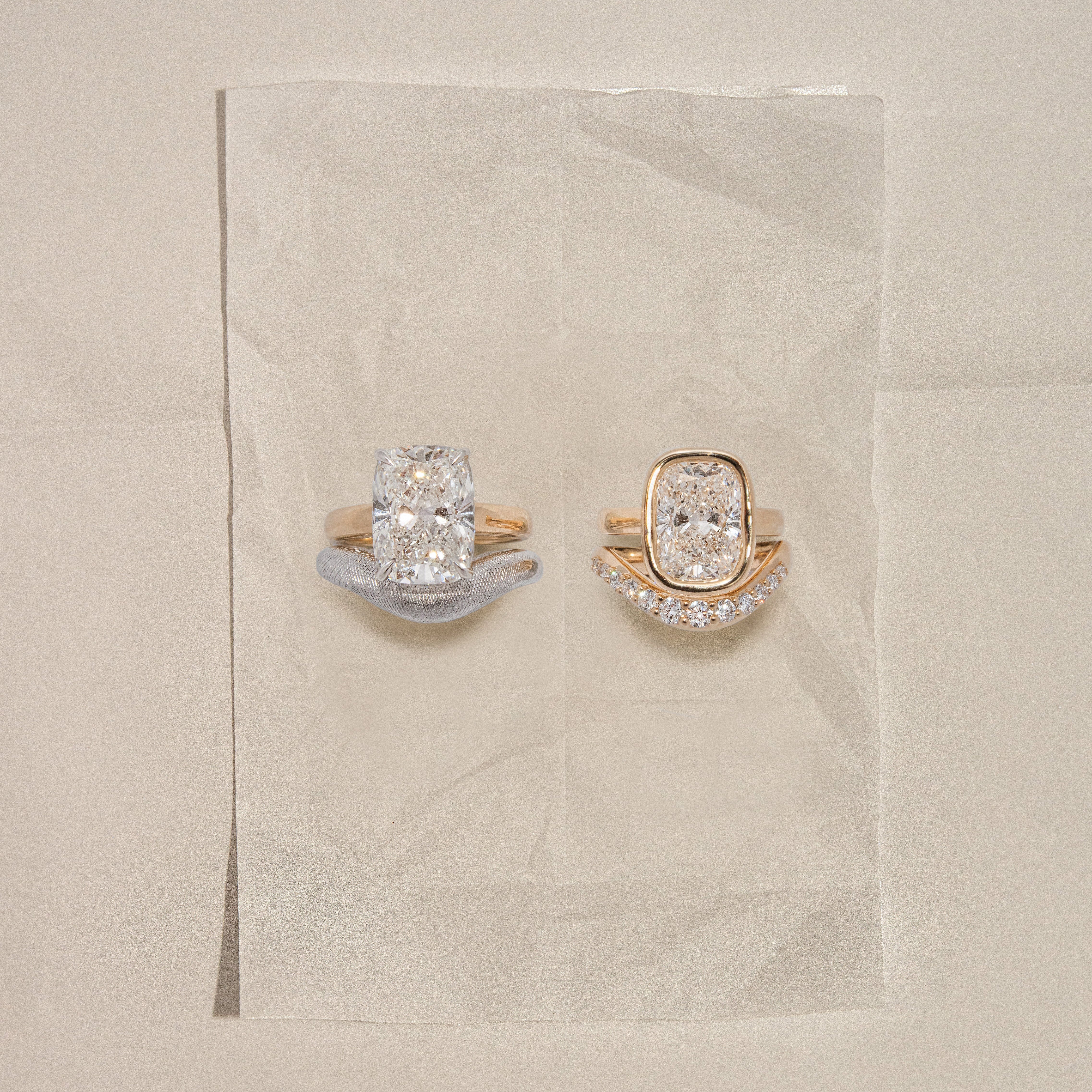 Two diamond rings on a beige fabric background