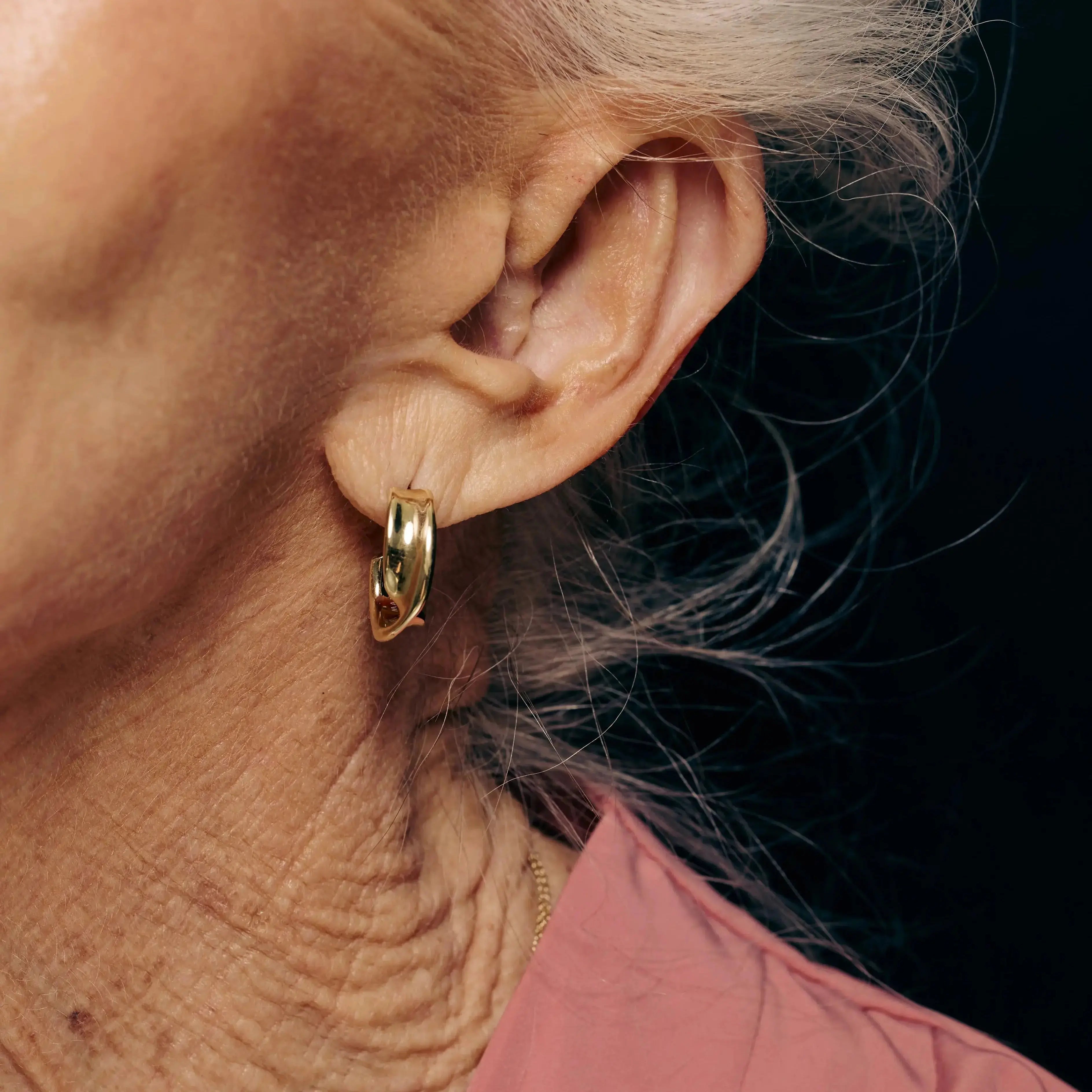 Close-up of an ear wearing a gold hoop earring with a dark background