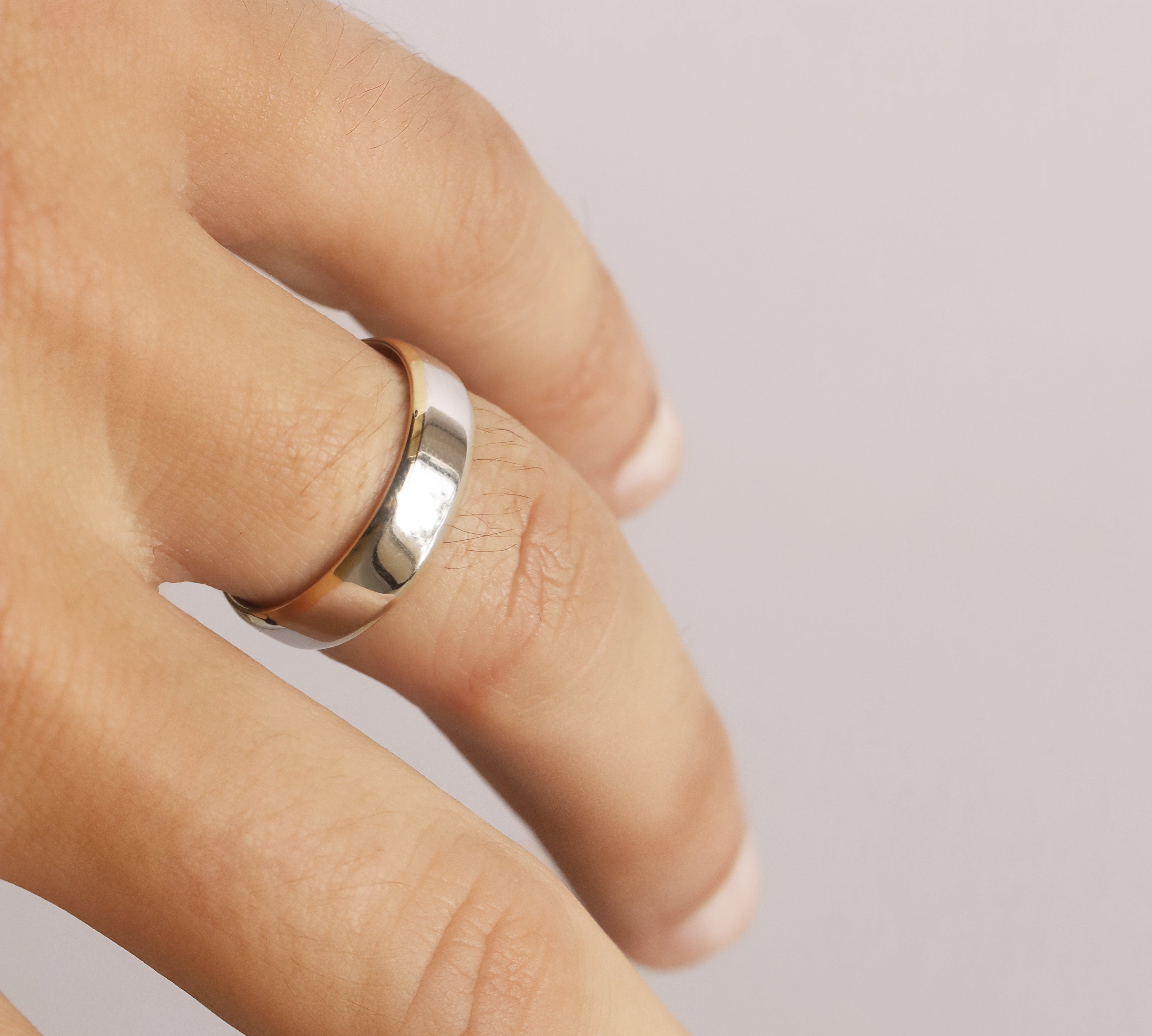 Close-up of a hand wearing a silver ring on a plain background