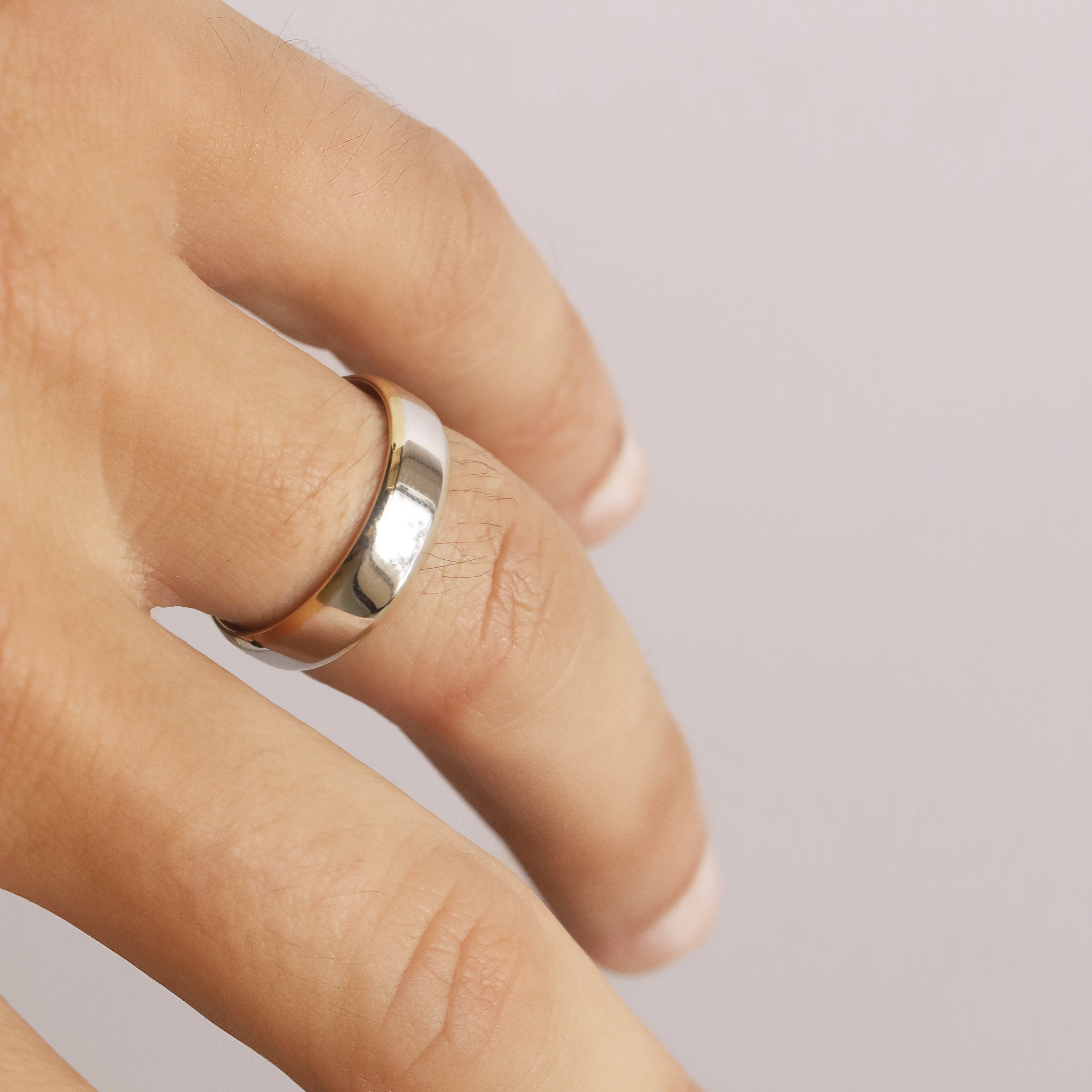 Close-up of a hand wearing a silver ring on a plain background
