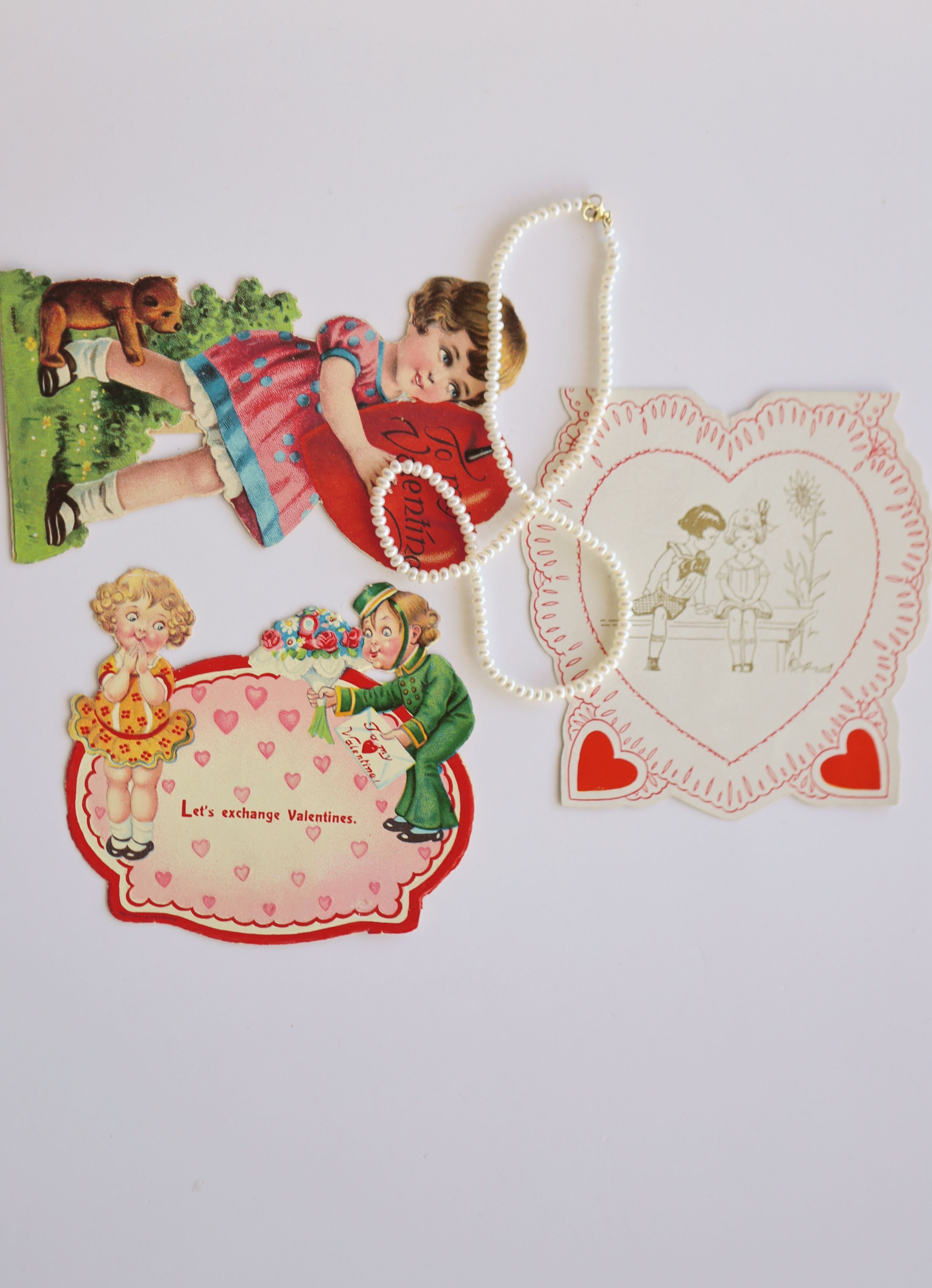 flat lay of 3 vintage valentine's day cards with pearl necklace against a white background