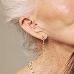 Close-up of a person wearing gold drop diamond earrings with a neutral background