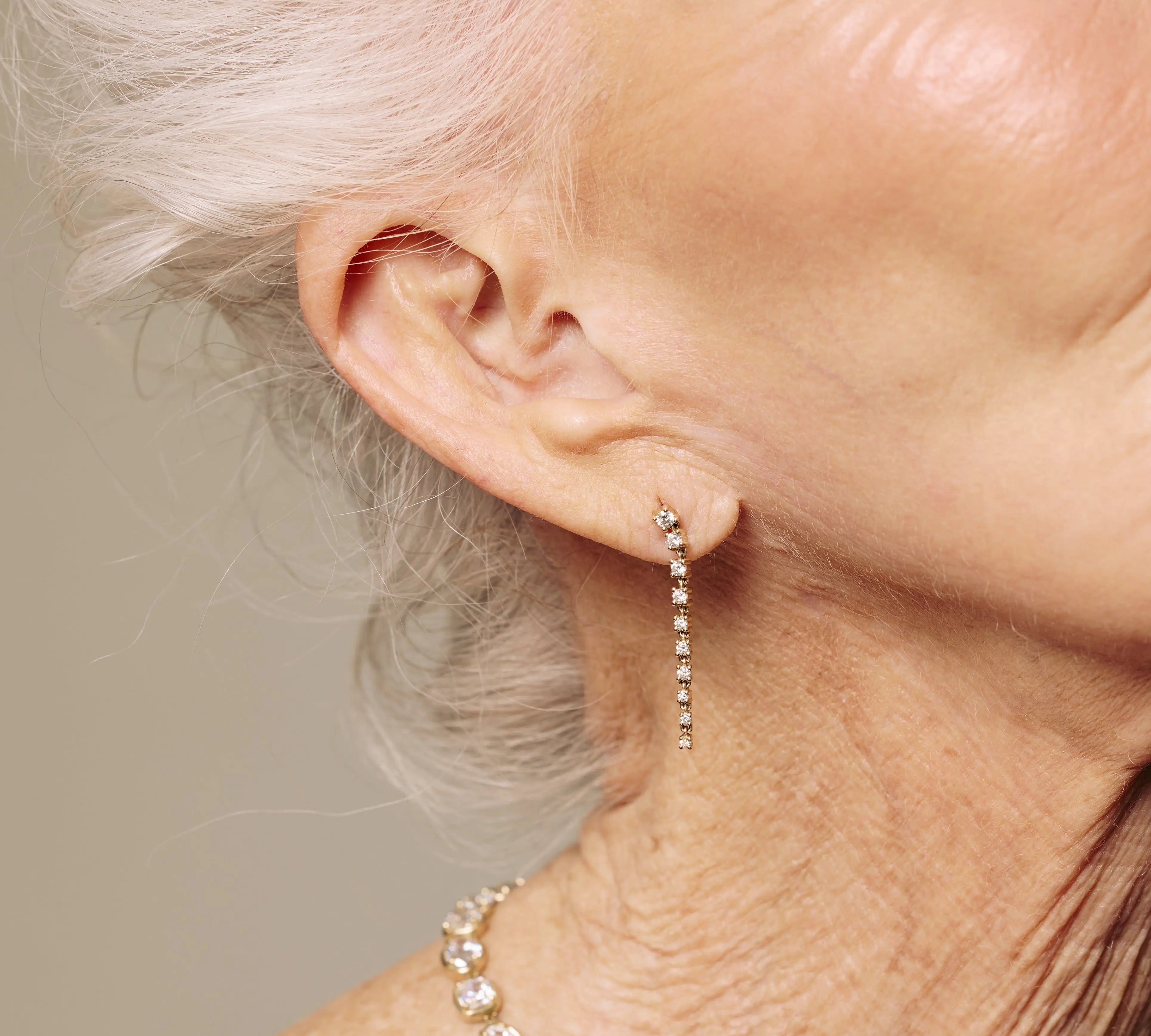 Close-up of a person wearing gold drop diamond earrings with a neutral background
