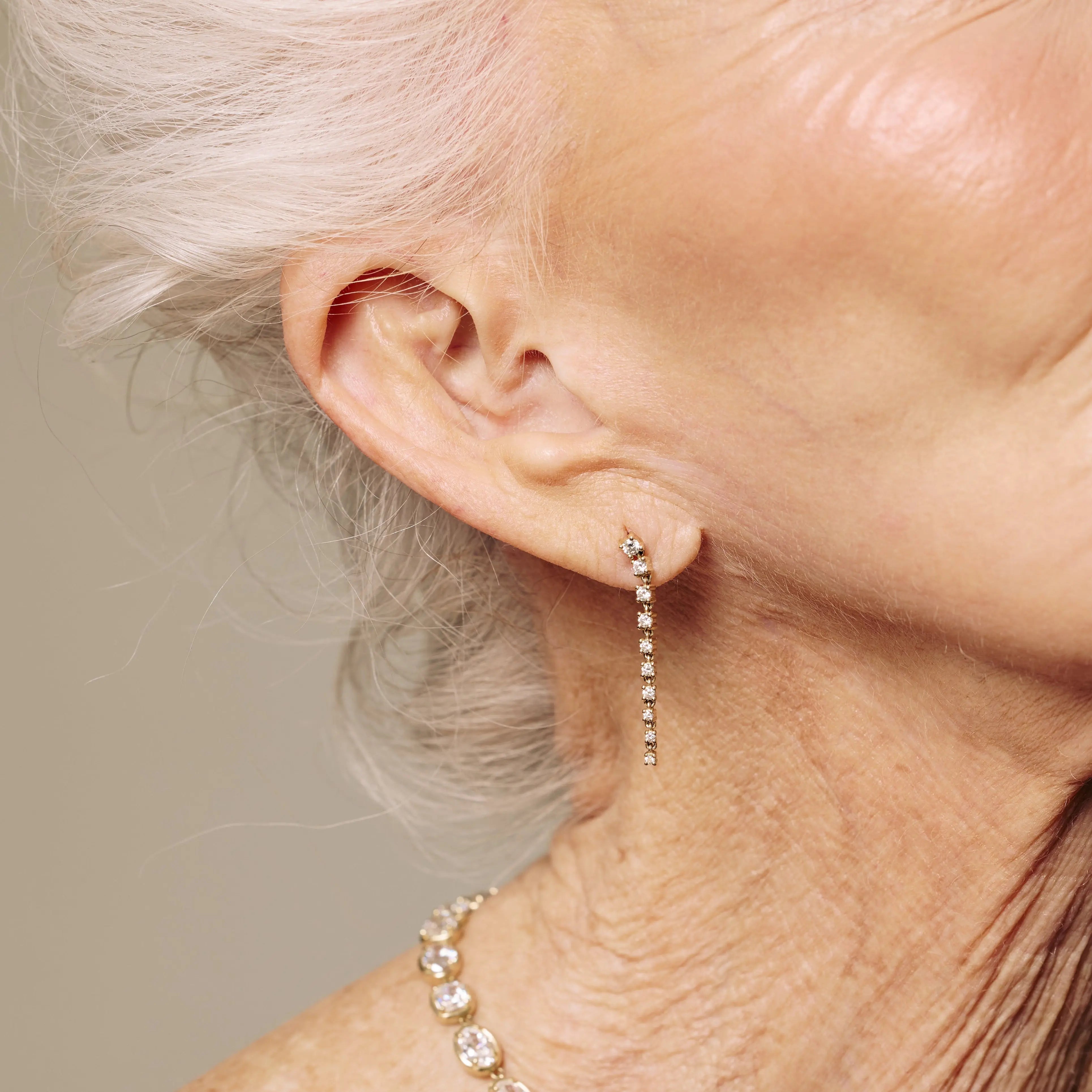 Close-up of a person wearing gold drop diamond earrings with a neutral background