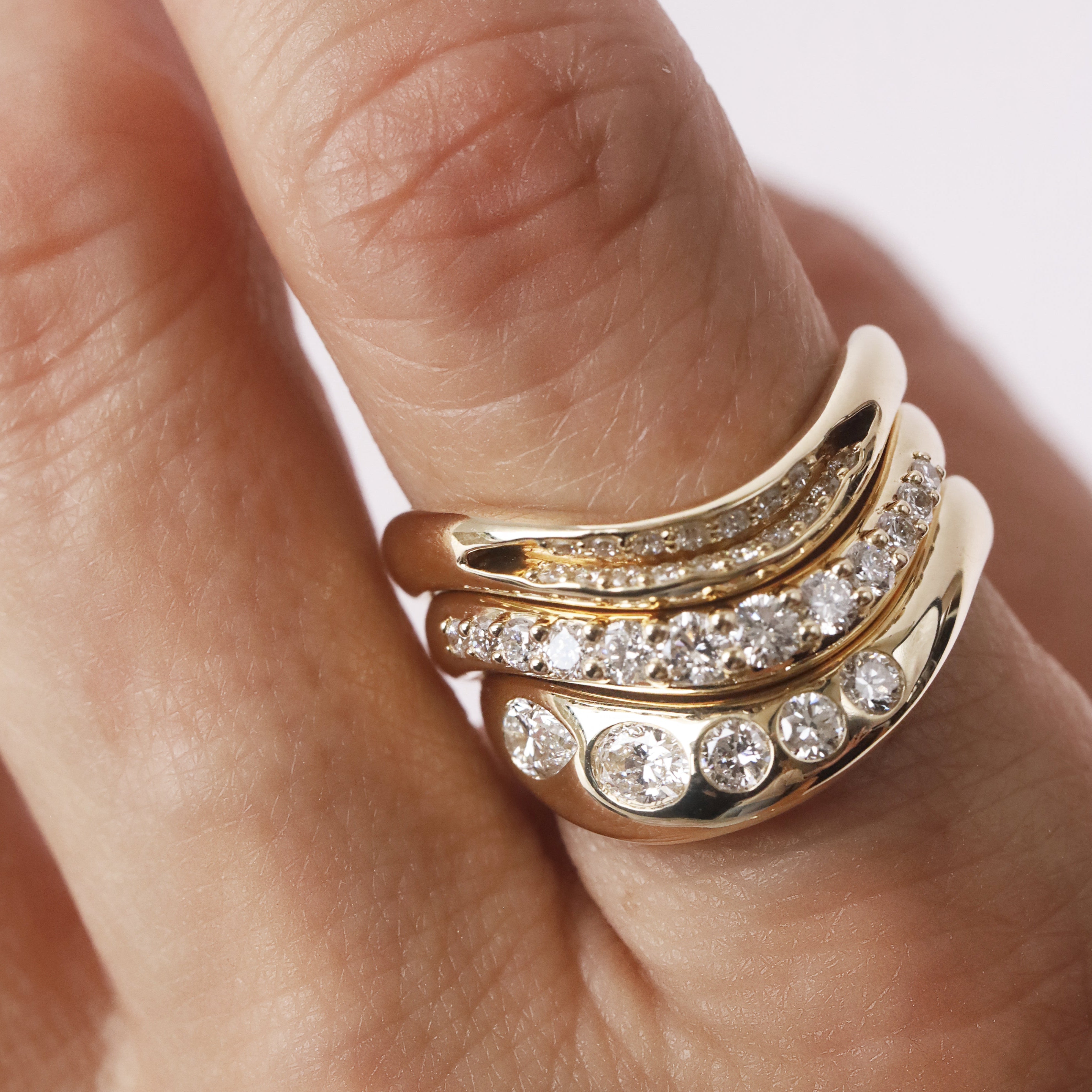 Gold ring with diamonds on a finger against a neutral background