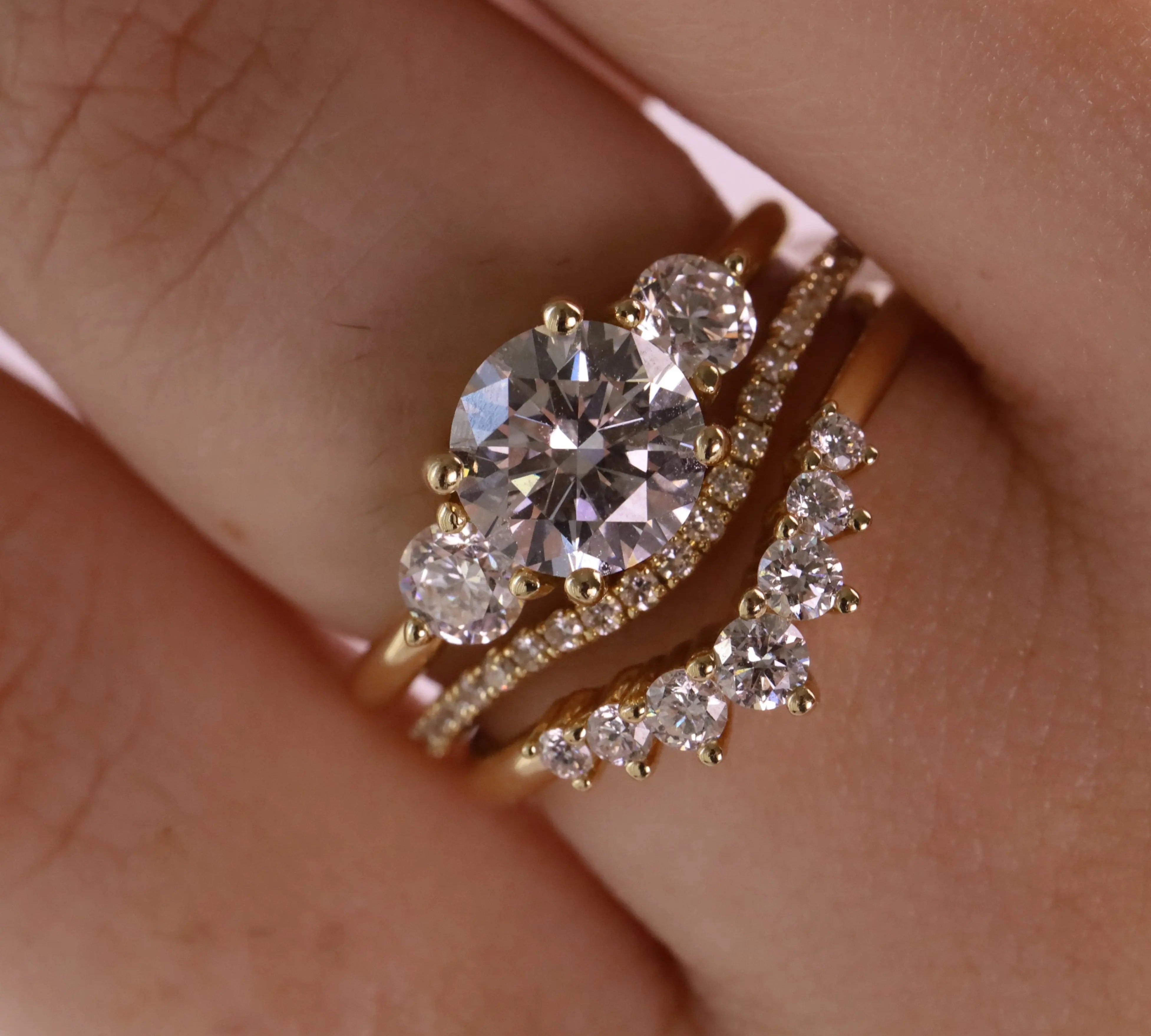 A close-up of a gold ring set on a finger, featuring a large oval-cut clear center stone with smaller round stones, alongside a curved diamond-accented band.