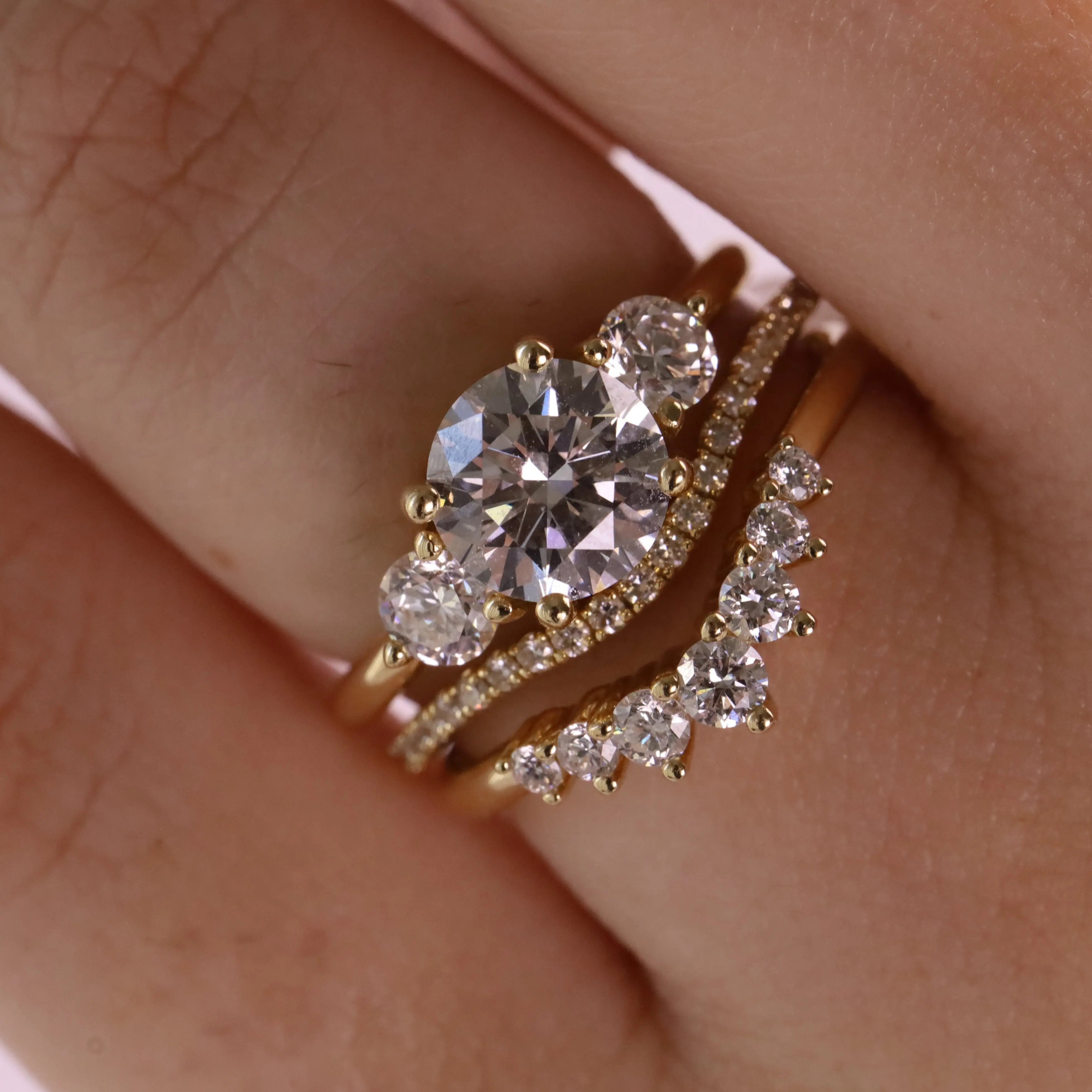 A close-up of a gold ring set on a finger, featuring a large oval-cut clear center stone with smaller round stones, alongside a curved diamond-accented band.