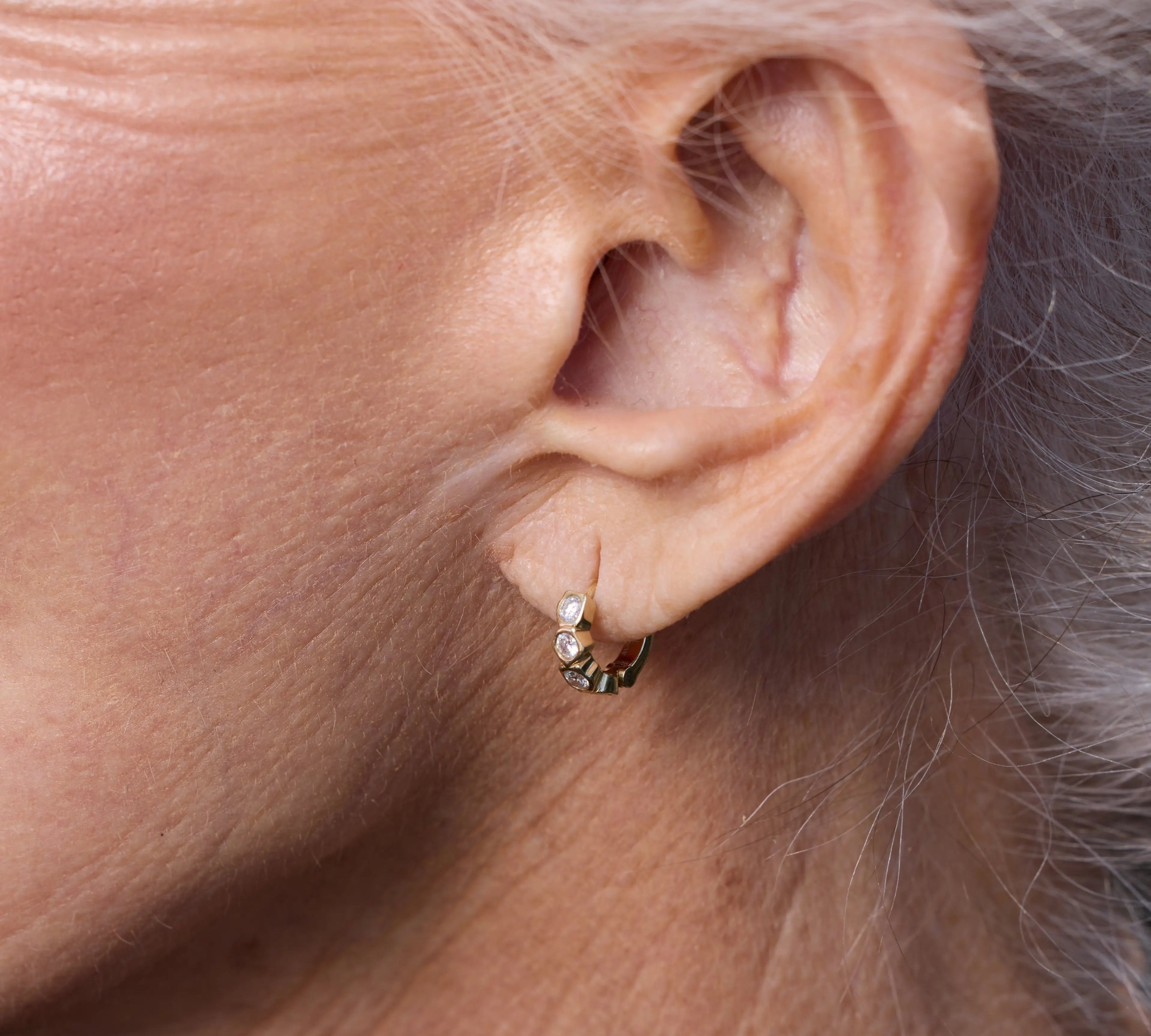 Close-up of an ear wearing a small earring with gray hair.
