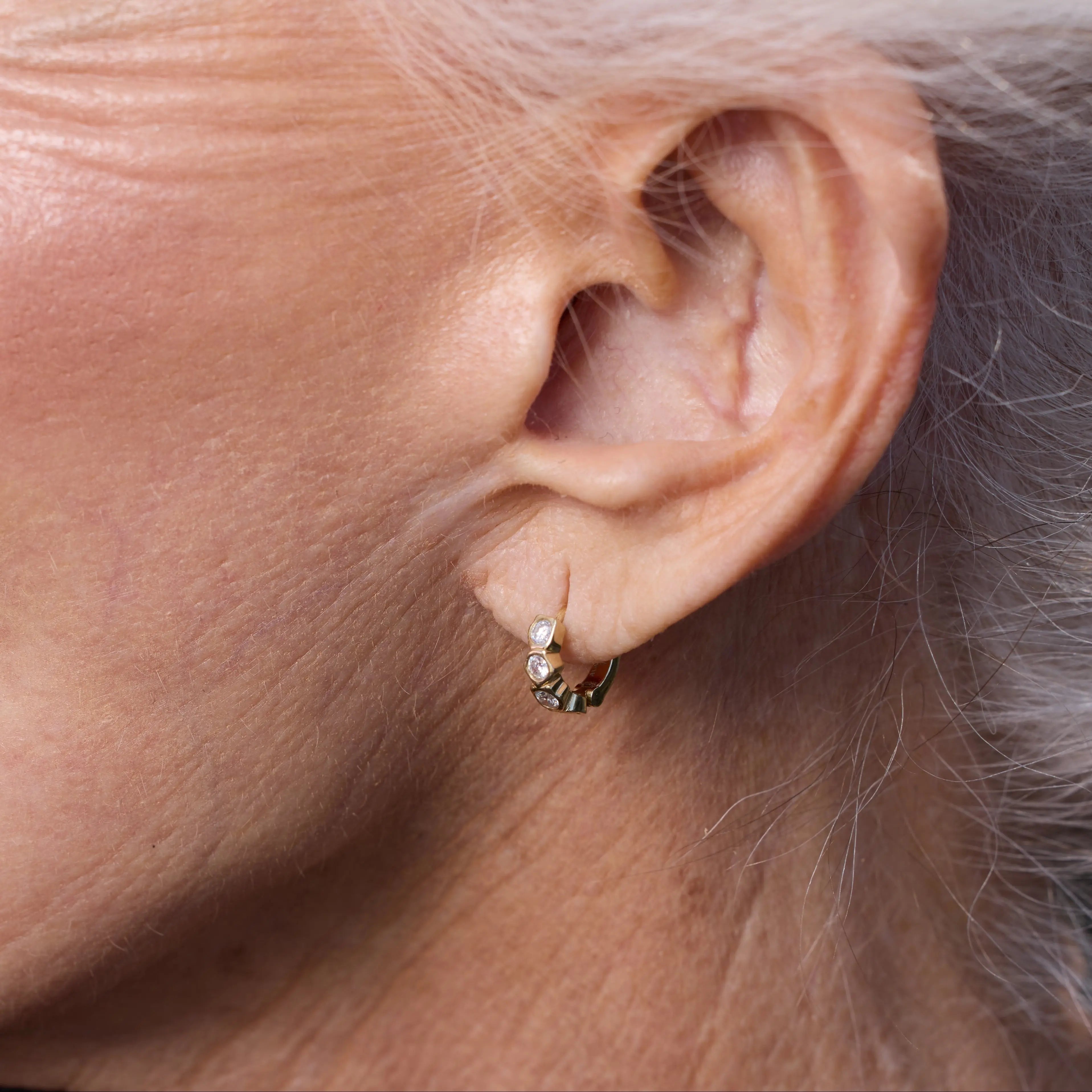Close-up of an ear wearing a small earring with gray hair.