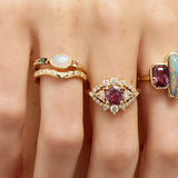 Close-up of fingers wearing multiple rings with gemstones on a light skin background