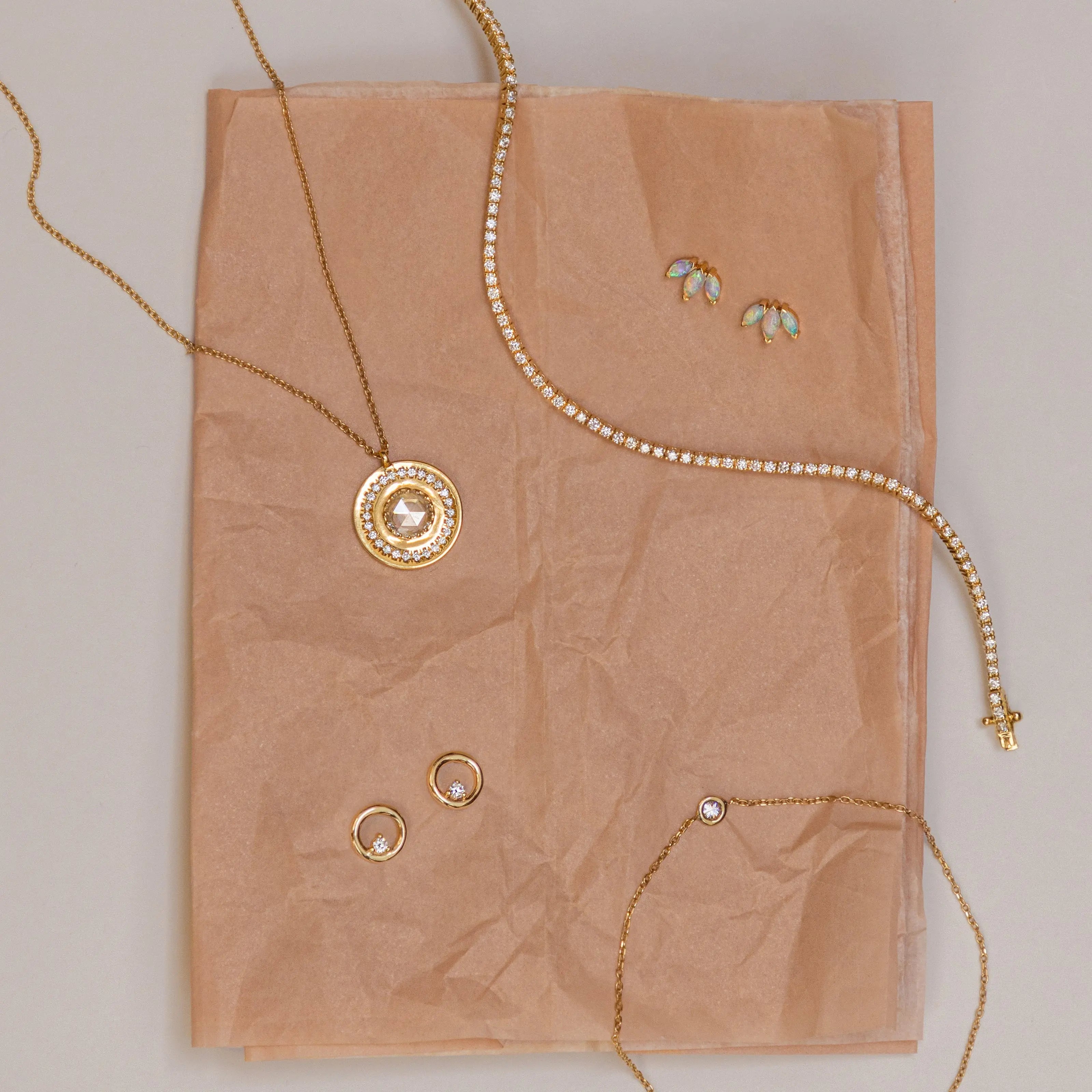 Flat lay on blush tissue paper: White Diamond La Femme pendant, Coco Tennis Bracelet, White Diamond Orbit Studs, Opal Lotus Studs and Dainty Diamond Bezel Bracelet