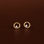 Gold earrings with circular design and embedded stones on a brown background