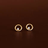 Gold earrings with circular design and embedded stones on a brown background