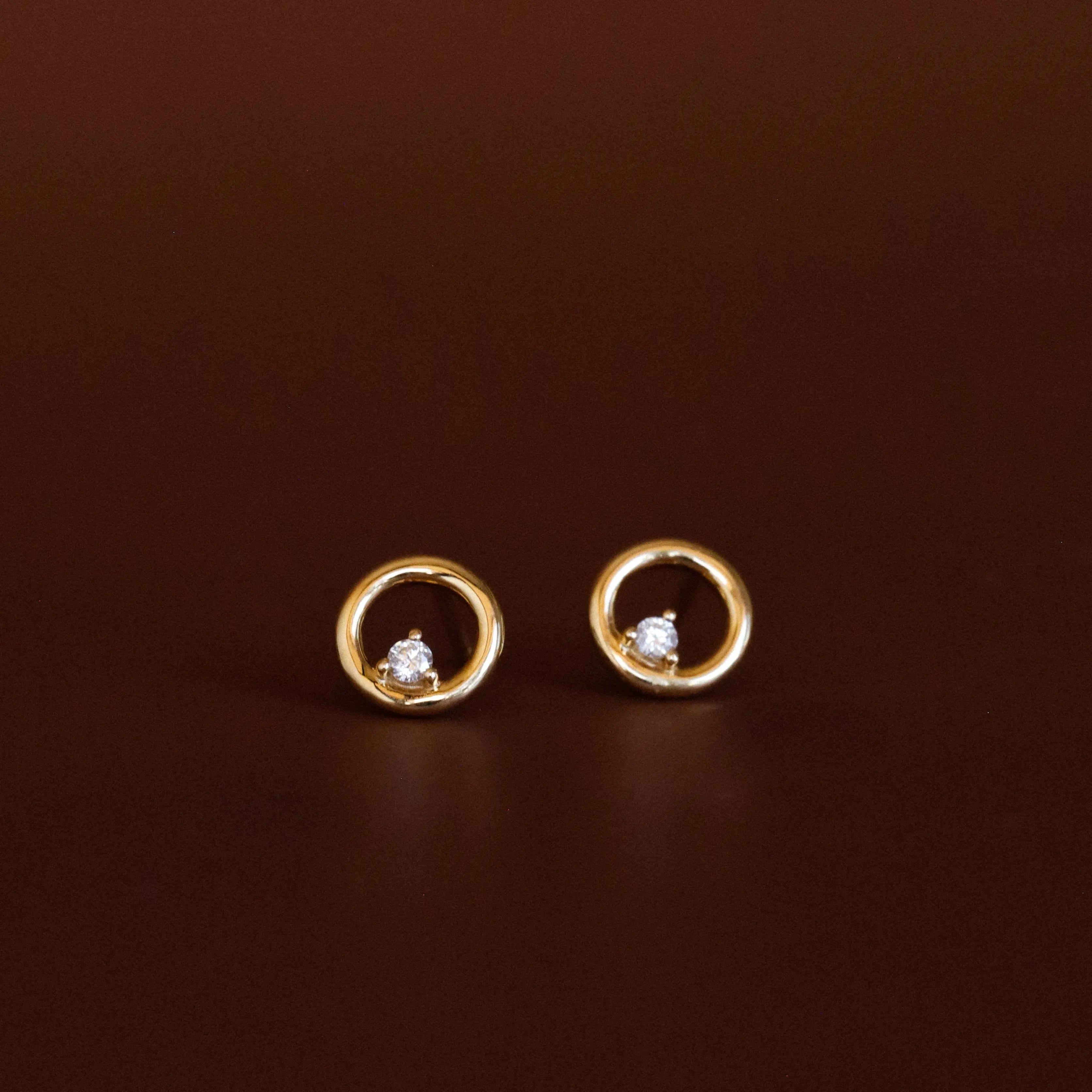 Gold earrings with circular design and embedded stones on a brown background